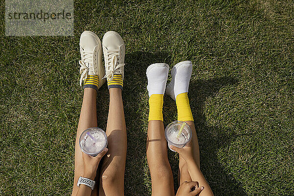 Mädchen in weißen Schuhen halten Milchshakes auf dem Gras im Park