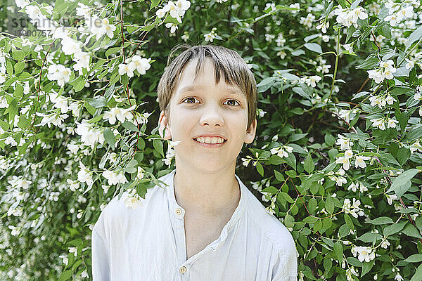 Smiling boy standing amidst plants with jasmine flowers