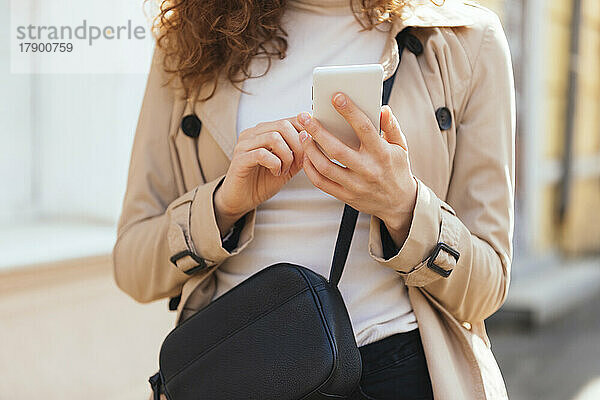 Frau im Mantel sendet Textnachrichten per Smartphone