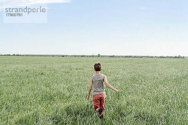 Boy running on grassy field by sky