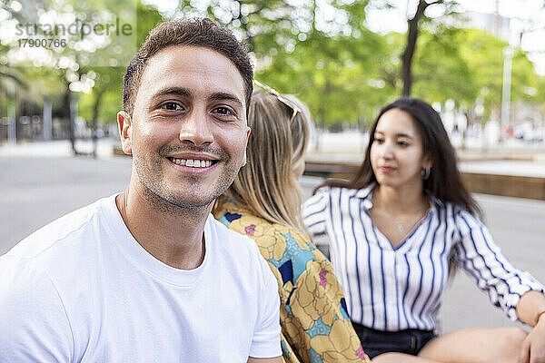 Lächelnder junger Mann sitzt mit Freunden im Park und unterhält sich