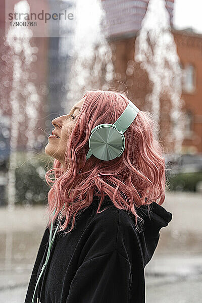 Smiling young woman with pink hair listening music through headphones