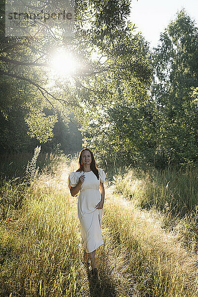 Frau in weißem Kleid steht an sonnigem Tag im Wald