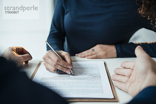 Geschäftsfrau unterzeichnet Dokument am Schreibtisch im Büro