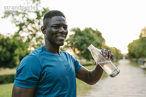 Lächelnder junger Mann hält Wasserflasche im Park