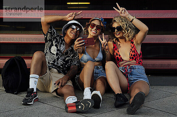 Junge Freunde machen Selfies per Smartphone und sitzen vor dem Fensterladen