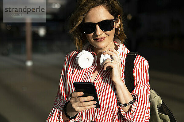 Lächelnde Frau mit Sonnenbrille und Smartphone
