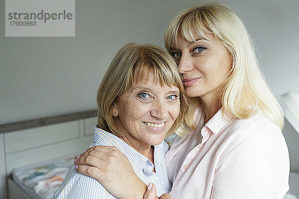 Lächelnde blonde Frau umarmt und fürsorglich ihre Mutter zu Hause
