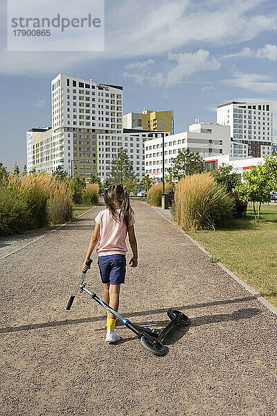 Mädchen mit Tretroller läuft auf Fußweg