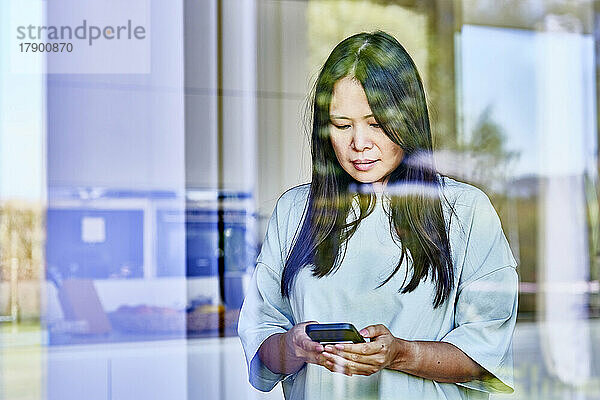 Frau benutzt Mobiltelefon  gesehen durch Glas