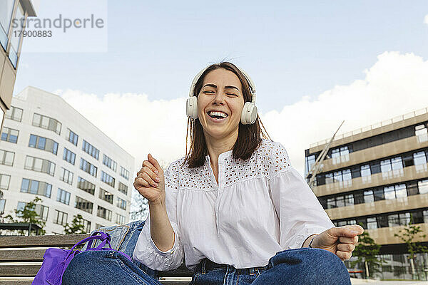 Sorglose Frau genießt Musik über kabellose Kopfhörer vor Gebäuden