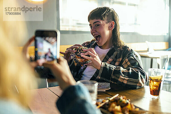 Junge Frau fotografiert Freundin mit Burger im Restaurant