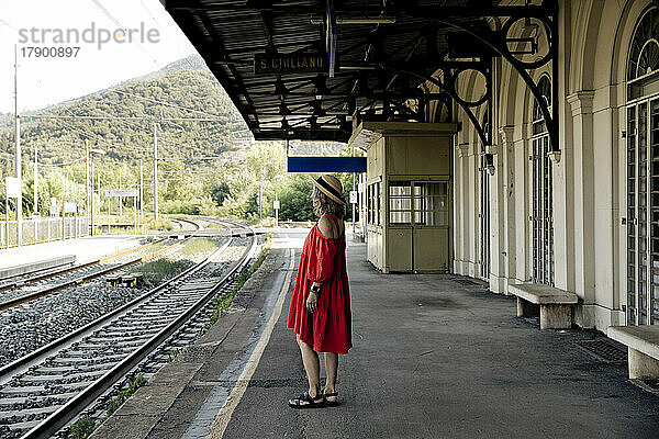 Frau im roten Kleid wartet am Bahnsteig auf den Zug