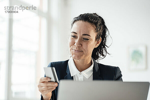 Lächelnde Geschäftsfrau mit Kreditkarte beim Online-Einkauf per Laptop