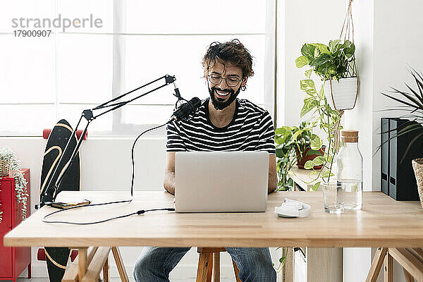 Glücklicher Mann mit Mikrofon und Laptop  der Podcast im Heimstudio aufnimmt