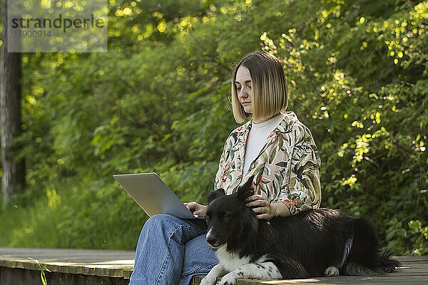 Junger Freiberufler arbeitet am Laptop mit süßem Hund im Park
