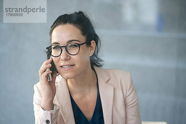 Geschäftsfrau telefoniert mit dem Mobiltelefon vor einer grauen Wand  die durch Glas zu sehen ist