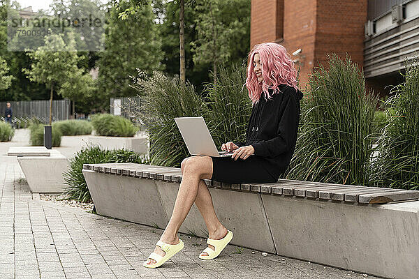 Smiling woman using laptop sitting on bench