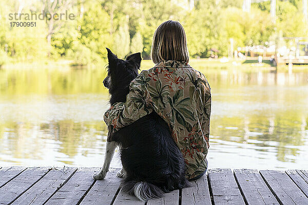 Junge Frau sitzt mit Hund am See im Park