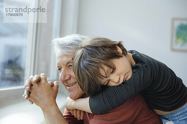 Nachdenklicher Junge umarmt Großvater zu Hause