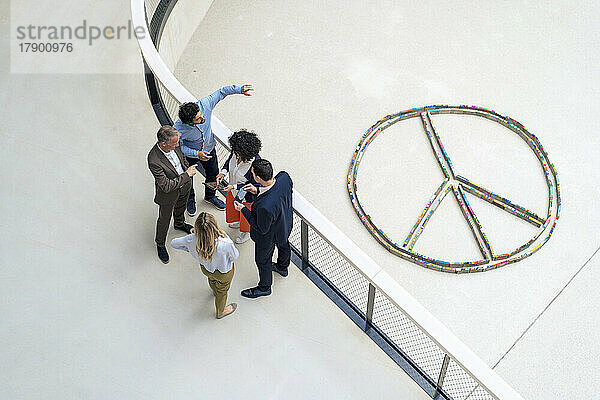 Multiracial business colleagues planning strategies by peace symbol in office corridor