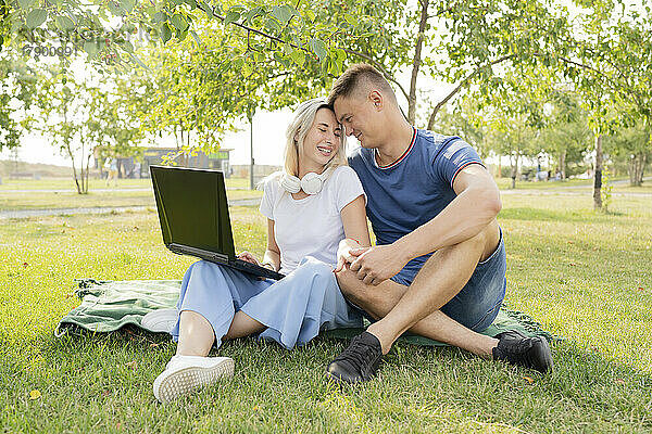 Liebevolle junge Frau und Mann mit Laptop verbringen ihre Freizeit im Park
