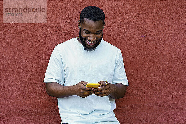 Lächelnder Mann benutzt Smartphone vor der Wand