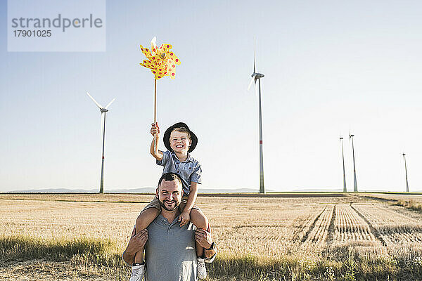 Vater trägt Sohn mit Windrad auf Schultern vor Windkraftanlagen