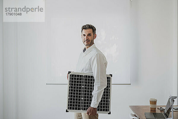 Lächelnder Ingenieur hält Solarpanel im Büro