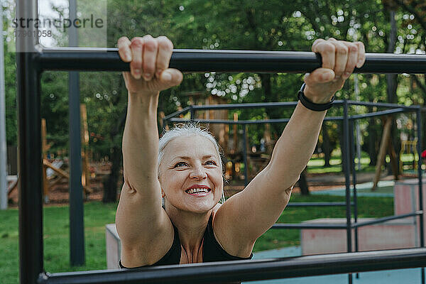 Glückliche reife Frau  die sich auf dem Spielplatz auf Stangen dehnt