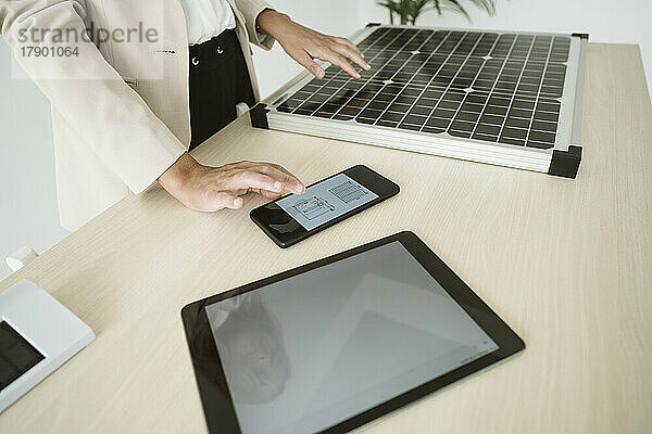 Frau im Büro mit Solarpanel auf Schreibtisch und Mobiltelefon