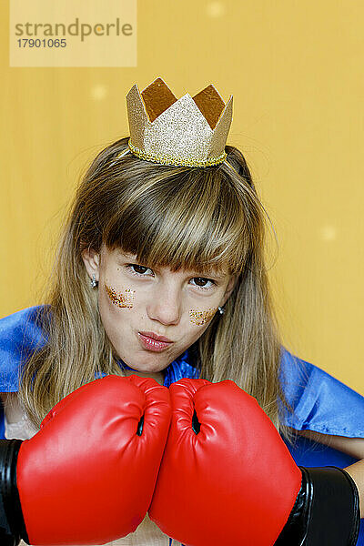 Girl in boxing gloves and crown against yellow background