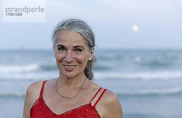 Glückliche ältere Frau mit grauen Haaren am Strand