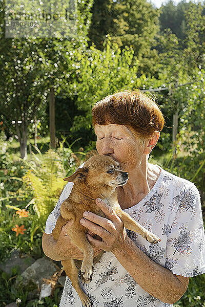 Ältere Frau küsst Hund im Garten
