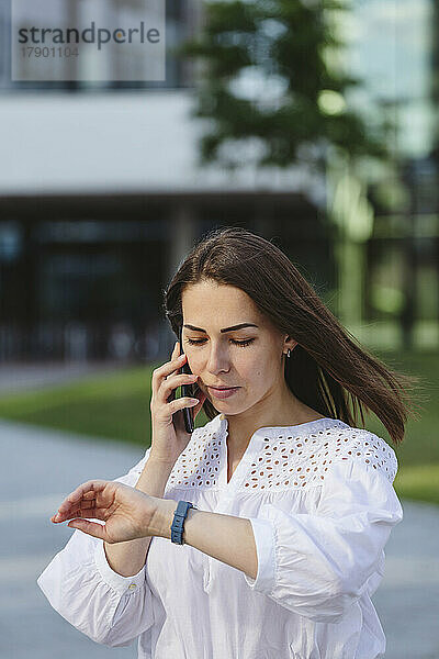 Geschäftsfrau überprüft die Uhrzeit mit einer Smartwatch und telefoniert mit dem Mobiltelefon