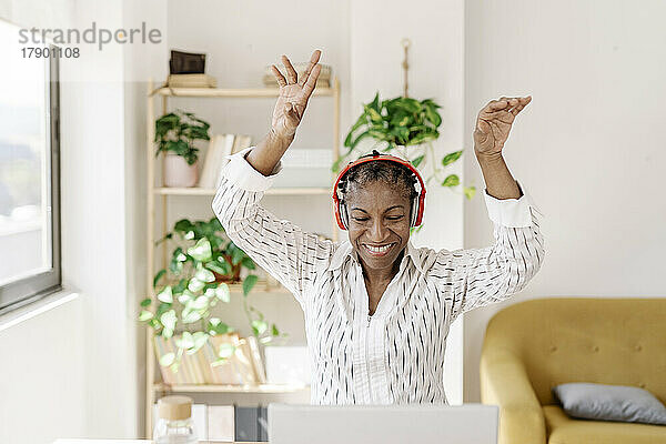 Glückliche Frau mit kabellosen Kopfhörern tanzt zu Hause