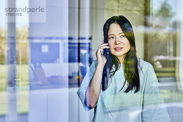 Reife Frau spricht mit Smartphone  gesehen durch Glas