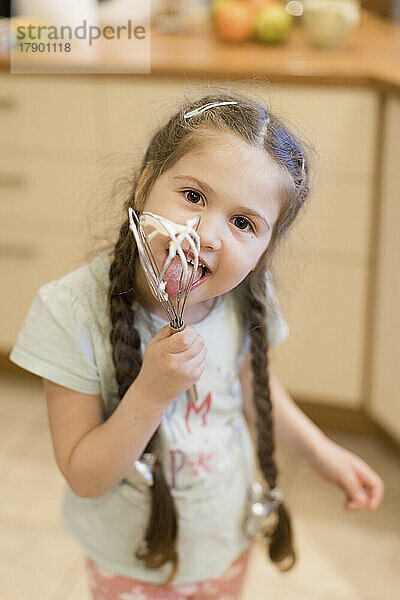 Portrait of little girl licking whipped cream off wire whisk