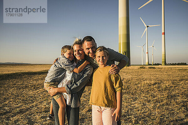 Happy family standing in wind park embracing children