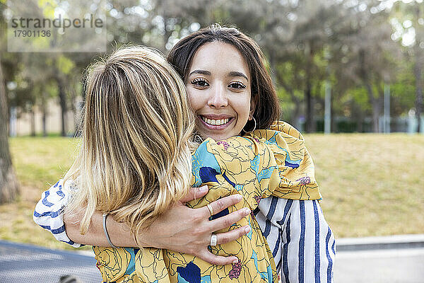 Glückliche junge Frau umarmt Freundin im Park