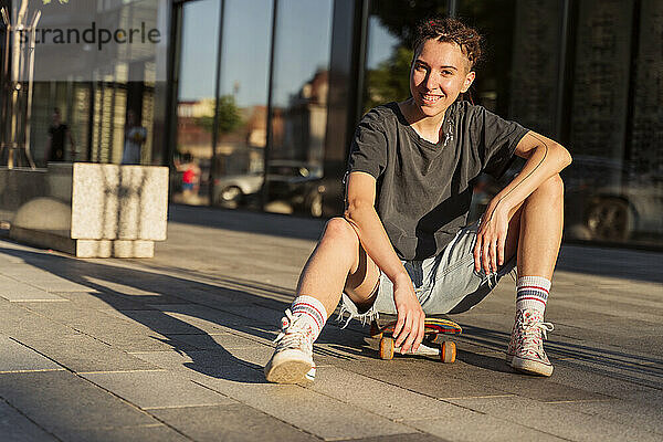 Lächelnde nicht-binäre Person  die auf einem Skateboard sitzt