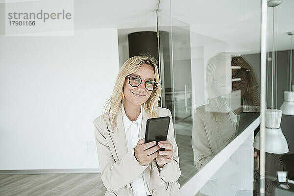 Selbstbewusste Geschäftsfrau mit Brille nutzt Mobiltelefon im Büro