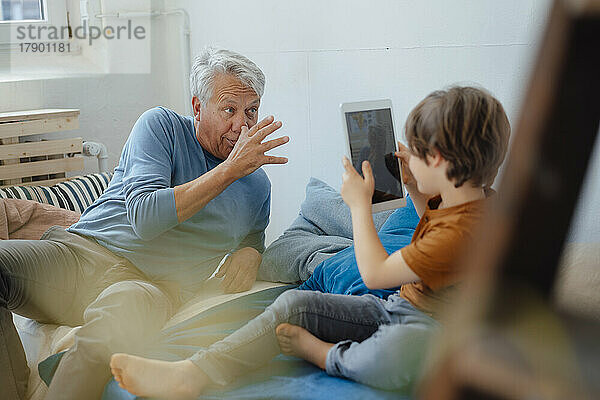 Junge fotografiert mit Tablet-PC den verspielten Großvater  der zu Hause neckt