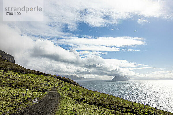 Färöer-Inseln  Vagar  Wolken über der unbefestigten Küstenstraße mit Inseln im Hintergrund