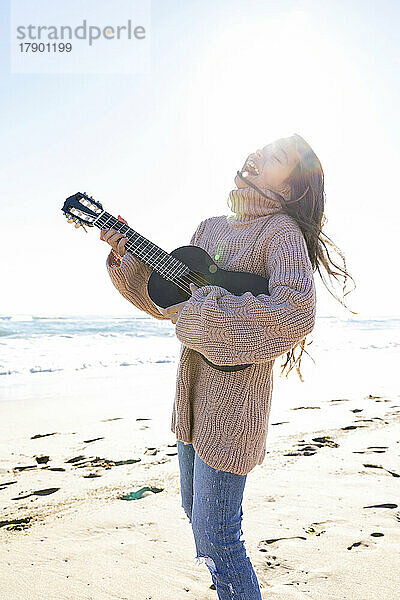 Fröhliches Mädchen  das am Strand Gitarre spielt
