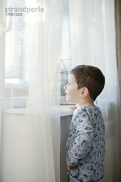 Junge im Schlafanzug schaut zu Hause durch das Fenster