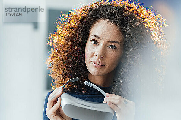 Geschäftsfrau mit lockigem Haar hält Virtual-Reality-Simulator in der Hand
