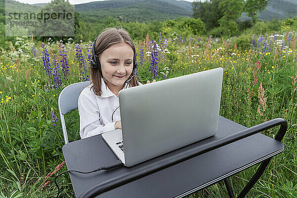 Lächelndes Mädchen beim Lernen per Videoanruf am Laptop auf der Wiese