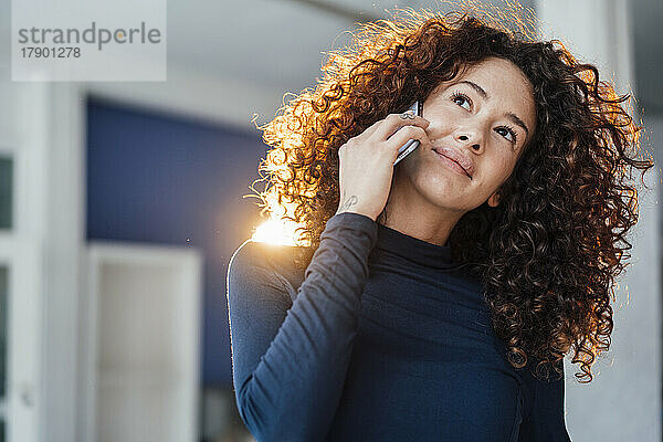 Nachdenkliche junge Frau mit lockigem Haar  die auf dem Smartphone spricht