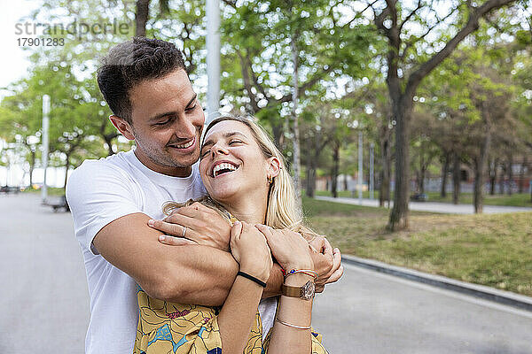 Happy man embracing cheerful girlfriend at park